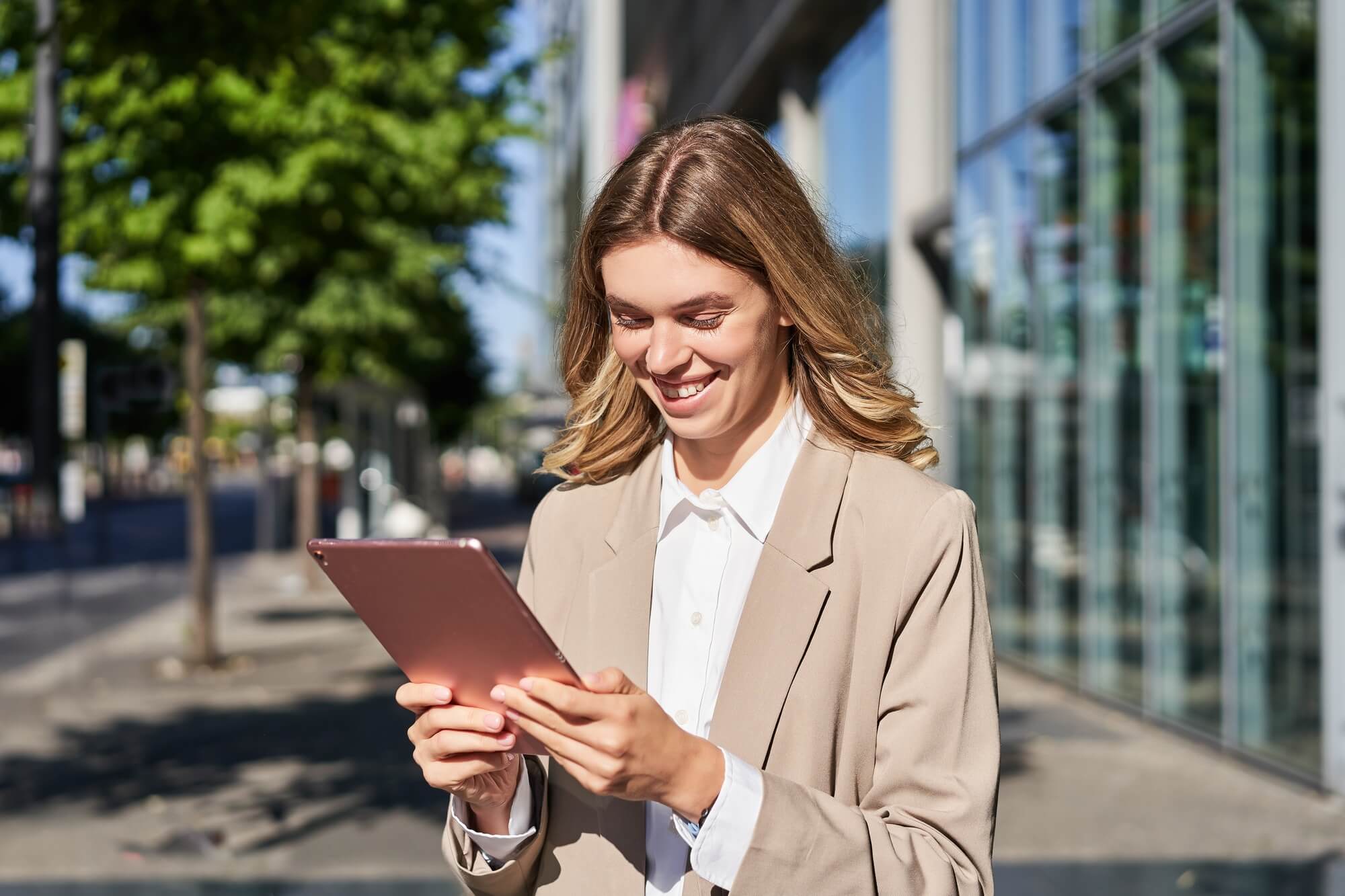 portrait-of-happy-businesswoman-smiling-holding-digital-tablet-on-street-near-office-building